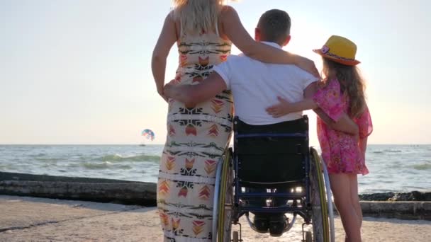 Инвалид с беременной женщиной и ребенком на заднем плане море, муж в инвалидной коляске — стоковое видео