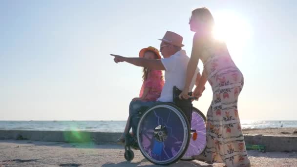 Parents avec enfant au repos, heureuse femme enceinte avec petite fille et personne handicapée en contre-jour fille s'assoit sur papa handicapé — Video