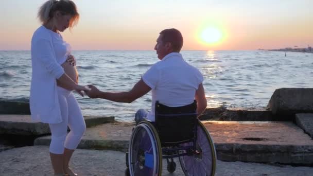 Pareja feliz, persona con discapacidad en silla de ruedas mantiene la mano de la chica embarazada — Vídeos de Stock
