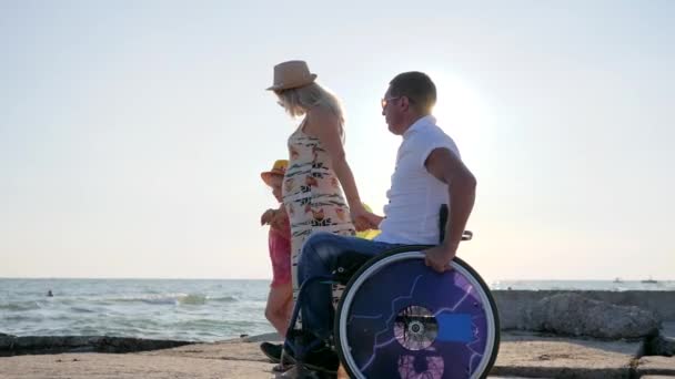 Счастливый инвалид папа ходить вместе с семьей рядом с морем в подсветке, ребенок с красочными воздушными шарами прогулки — стоковое видео
