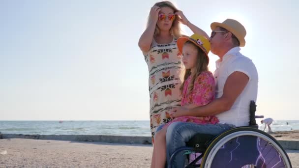 Feliz familia se comunica en el fondo cielo azul y la costa del mar, discapacitado con la esposa embarazada y abrazo hija — Vídeos de Stock