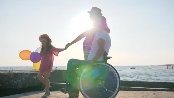 Lycklig familj, Handikappad i rullstol promenad med gravid fru, barn håller luftballonger och hoppa, invalid med fru — Stockvideo