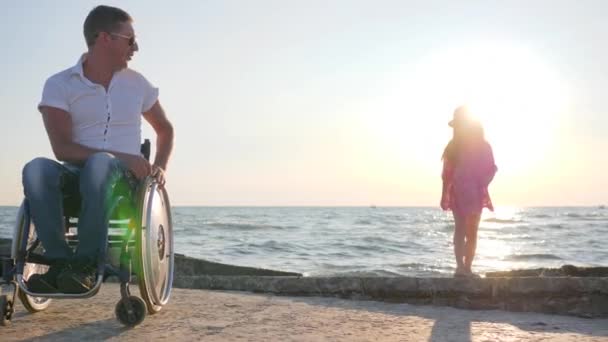 Vammainen mies pyörätuolissa katsoo hyppäämällä lapsi taustavalossa lähellä merta hidastettuna suosionosoituksia tytär — kuvapankkivideo