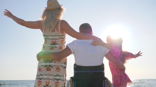 Man i rullstol kram fru och liten flicka i bakljus, funktionshindrade kramar sin fru och dotter, ogiltig — Stockvideo