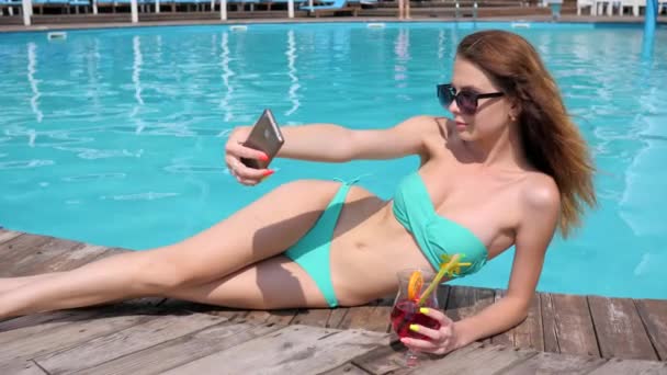 Fotos aus dem Urlaub, Mädchen macht Foto am Handy, Frau macht Selfi im Badeanzug mit buntem Cocktail