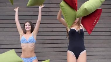 Mayo giymiş güzel kızlar yastık fırlatıyor, gülen arkadaşlar arka plandaki tahta duvarda eğleniyorlar.,