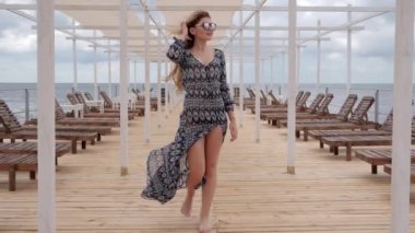 young woman glasses walks on wooden pier, Expensive holidays of women on coast ocean, female in sunglasses