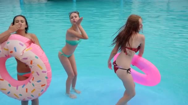 穿着泳衣的好朋友们带着蓝色的水跳着舞走进游泳池，夏天，快乐的姑娘们带着粉色的充气环 — 图库视频影像