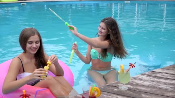 Amigos Em roupa de banho descansando na piscina, festa de verão, namoradas em maiôs Bolhas de sabão de sopro na piscina , — Vídeo de Stock