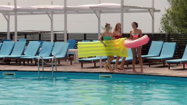 Подружки в купальному костюмі стрибають з дерев'яного пірсу в басейн з блакитною водою, дівчата відпочивають біля басейну — стокове відео