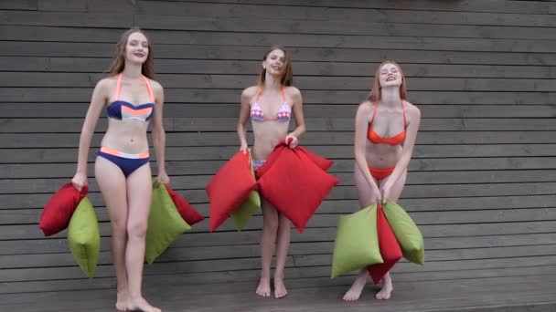 수영복을 입은 여자 친구들 이 여러 가지 색깔의 쿠션을 공중으로 던진다. 수영복을 입은 아리따운 여자들 이 베개를 던진다., — 비디오
