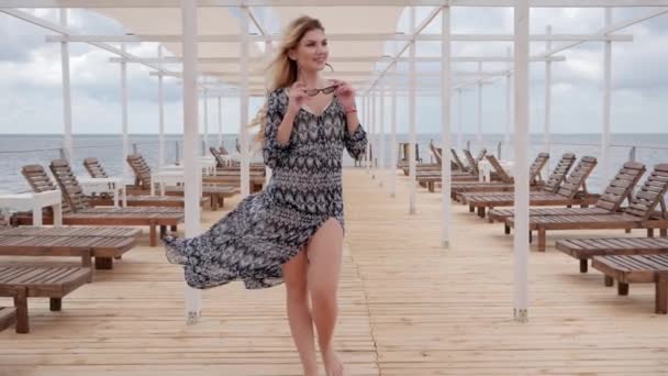 Długowłosy dziewczyna w rozwoju ubrania na nabrzeżu, młoda kobieta w okularach spacery po drewnianym molo, drogie wakacje — Wideo stockowe