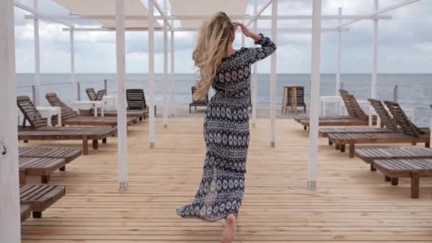 Счастливая женщина зовет ее, летние каникулы женщин на берегу моря, девушка в разработке одежды на ветру на набережной, молодая женщина идти босиком — стоковое видео