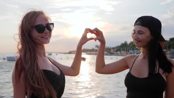 Kvinna gör hjärta händer på bakgrunden havet, flickor tittar på kameran och visa hjärta på vallen — Stockvideo