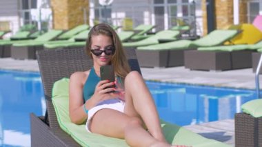 Mayolu ve güneş gözlüklü genç çekici bir kadın tatil sırasında pahalı otellerde dinlenirken cep telefonuyla selfie çekiyor.