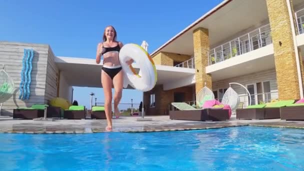 Vrolijk vormgegeven vrouw in badpak met opblaasbare ring sprong in het zwembad in dure resort tijdens de zomervakantie, onderwater schieten — Stockvideo