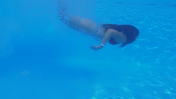 Chica delgada piernas largas con hermosas inmersiones en el cuerpo y nada bajo el agua en la piscina azul claro durante las vacaciones de verano en el complejo, tiro bajo el agua — Vídeo de stock