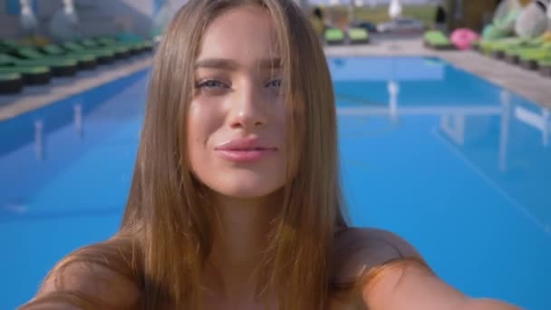 Vacanze estive selfie foto e video sul cellulare, giovane donna attraente si spara sulla macchina fotografica sullo sfondo della piscina blu in località costosa durante le vacanze — Video Stock