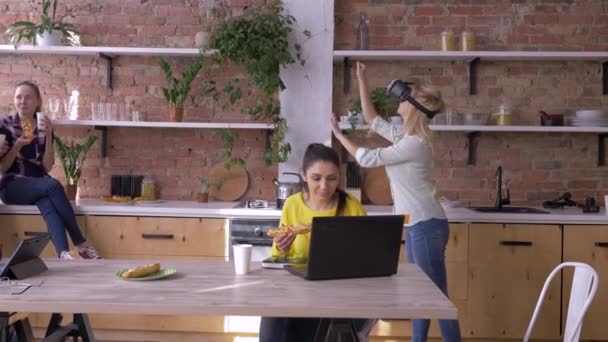 L'avenir est maintenant, jeune femme avec des lunettes de réalité virtuelle joue à des jeux pendant que les collègues mangent et communiquent tout en travaillant dans un bureau moderne — Video