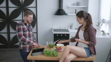Neşeli komik çocuk ve kız, kahvaltıda sağlıklı sebze salatası pişirirken cep telefonuyla selfie çekiyorlar.