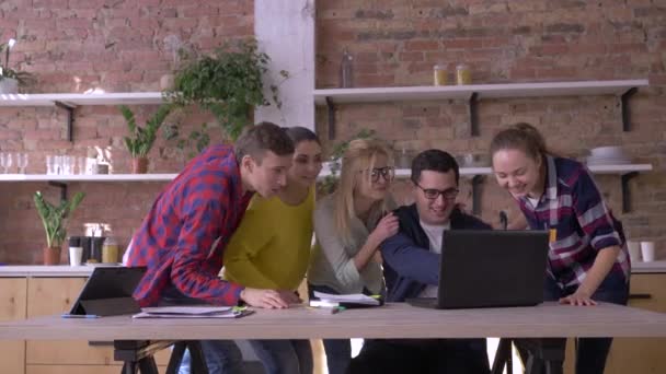 Erfolgreiches Geschäft, Bürokater in Brille lernt gute Nachrichten am Computer und freut sich mit Kollegen, die sich im Büro umarmen und Dokumente in die Luft werfen — Stockvideo