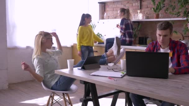 úspěšný tým mladých podnikatelů jedí a pracuje s tabletami a notebooky v kuchyni během kreativního projektu v moderní kanceláři