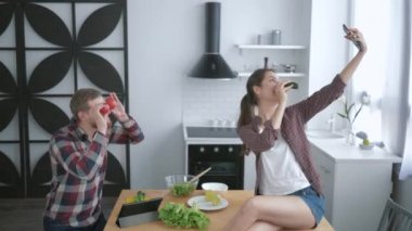 Çılgın bir aile, komik, neşeli bir adam etrafta dolanıp sebzelerle surat asıyor ve kadınlar sağlıklı yemek pişirirken akıllı telefonlarıyla fotoğraf çekiyor.