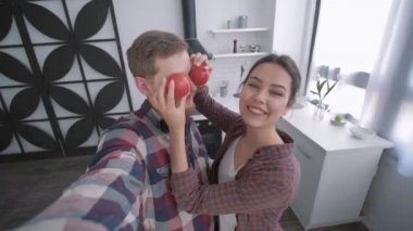 Kadınlı çılgın bir adam akıllı telefondan selfie videosu çeker ve sağlıklı beslenmek için kahvaltıda sağlıklı yemekler pişirirken sebzelerle vakit geçirir.