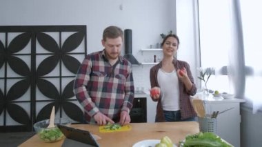 Eğlenceli yemek pişirme, erkek dansı yapan neşeli kadın ve akşam yemeğinde sağlıklı olmak için sebze salatası pişirirken beslenme planına göre