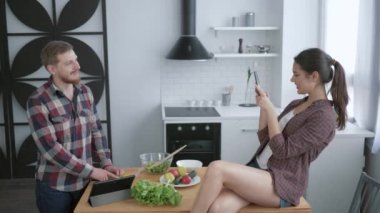 Akşam yemeği için sağlıklı sebze salatası pişirirken cep telefonuyla selfie çeken eğlenceli genç bir çift.