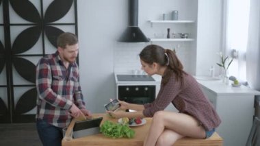 Sağlıklı yemek, neşeli kadın akıllı telefondan adamın mutfakta hazırladığı sağlıklı diyet sebze salatasının fotoğrafını çeker.