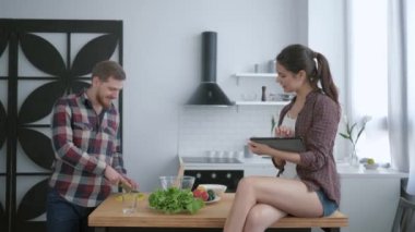 Sağlıklı yemek, genç adam öğle yemeğinde faydalı bir vejetaryen, elinde tabletle mutfak masasında oturan bir kadın ve yemek pişirme tavsiyesi hazırlar.