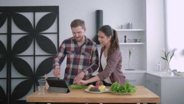 Dieta saludable, mujer feliz con el hombre prepara alimentos saludables de verduras y verduras de acuerdo con el plan de dieta para el bienestar en la mesa de la cocina utilizando tableta con video enseñanza — Vídeos de Stock