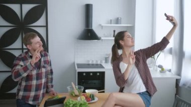 Sağlıklı yaşam tarzı, mutlu aile cep telefonuyla selfie çekerken mutfakta taze sebze ve sebzelerden sağlıklı yiyecekler hazırlıyor.