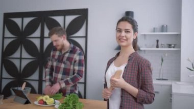 Mutfakta gülümseyen mutlu bir kızın portresi. Tatmin olmuş bir kadın, yemek masasında tablet kullanarak sebzelerden yararlı sağlıklı yiyecekler hazırlayan adama bakıyor.
