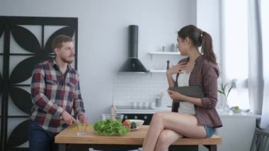 Faydalı yemek, mutlu adam yemekte sağlıklı vejetaryen yemeği hazırlar ve kız elinde tabletle mutfak masasında oturur ve iletişim kurar.