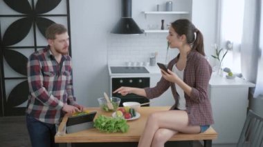 Kilo normalleştirme, erkek kahvaltıda sağlıklı vejetaryen salatası hazırlar ve kadın elinde akıllı telefonuyla mutfak masasında oturur ve selfie çeker.