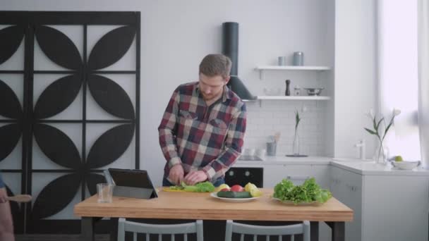 Peso saludable, esposa feliz con el marido prepara alimentos saludables de verduras y verduras de acuerdo con el plan de dieta para el bienestar en la cocina utilizando tableta moderna con video lección — Vídeos de Stock