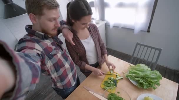 남자와 결혼 한 여자 아이는 부엌에서의 다이어트 계획에 따라 건강을 위해 저녁으로 야채 샐러드를 요리하면서 핸드폰으로 셀카 사진을 찍는다. — 비디오