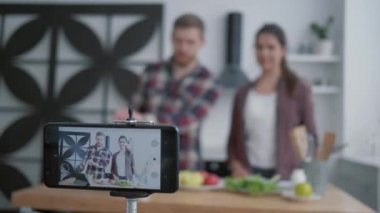 Sağlıklı yaşam tarzı, blog yazarları kadın ve erkek mutfakta sebzeler ve yeşilliklerle yararlı bir öğle yemeği hazırlarken, kamera akıllı telefon sosyal ağlardaki abonelerin videolarını kaydediyor.
