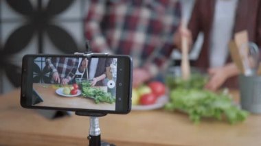 İnternet video blogu, akıllı telefon takipçileri için video çekiyor. Kadın ve erkeğin mutfağa yakın taze sebze ve yeşilliklerden nasıl sağlıklı yemekler pişirdiklerini anlatıyor.
