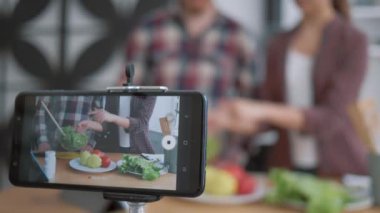 Zayıflatıcı diyet blogu, cep telefonu video kaydını canlı kılıyor. Kadın ve erkek blogcuların taze sebze ve sebzelerden sağlıklı gıdaları nasıl hazırladıklarını gösteriyor. Diyet planına göre mutfağı kapatın.