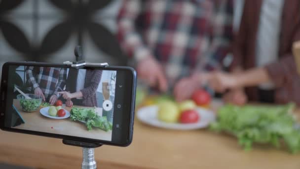 Blogs online, celular faz vídeo para assinantes como blogueiros casal cozinham preparando refeições saudáveis a partir de vegetais frescos e verduras perto na cozinha — Vídeo de Stock