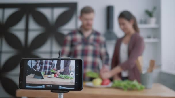 Aprendizaje en línea para cocinar alimentos saludables, jóvenes bloggers pareja enseñar a los suscriptores a cocinar alimentos útiles de verduras para la normalización del peso y el bienestar, mientras que los registros de teléfonos inteligentes video tutorial — Vídeos de Stock