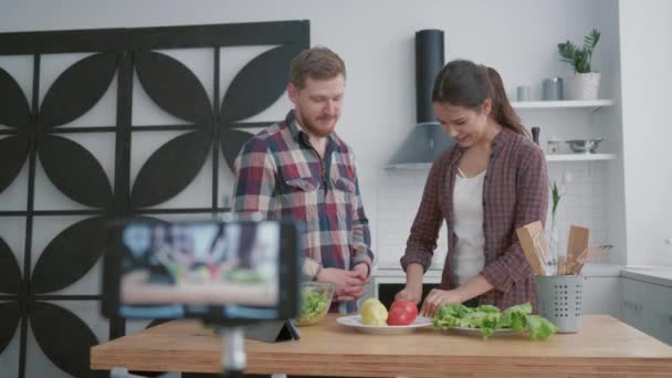 Lección en línea para culinaria, bloggers felices chico y chica enseñar a los suscriptores a cocinar alimentos útiles de verduras para la normalización del peso y el bienestar, mientras que los registros telefónicos video tutorial — Vídeos de Stock