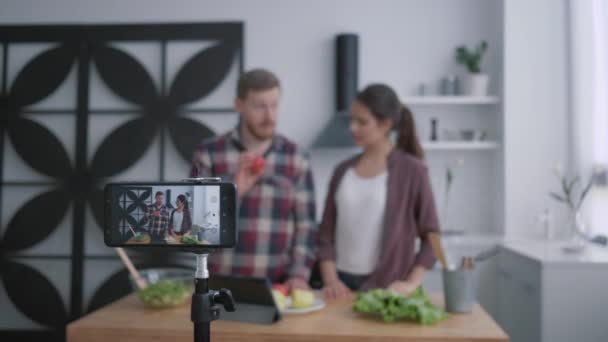 Vegan blog, vloggers τύπος και κορίτσι ετοιμάζουν υγιεινό φαγητό με λαχανικά και χόρτα στην κουζίνα, ενώ κάμερα smartphone καταγράφει βίντεο για τους οπαδούς στα κοινωνικά δίκτυα — Αρχείο Βίντεο