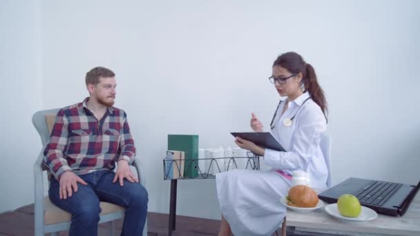 Dietoloji, sakallı çekici müşteri erkek doktor diyetisyen hekime parlak bir hastanede oturup kilo kaybı ve sağlıklı beslenme hakkında danışmanlık yapıyor. — Stok video