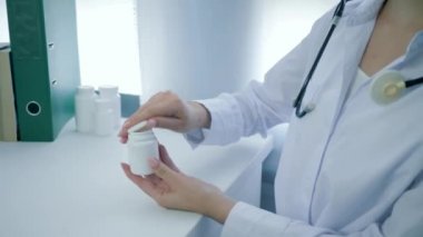 Diyetisyen eller vitamin şişesini açar ve sarı yuvarlak hapları beyaz masaya döker.