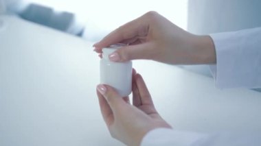 Besin takviyeleri, beslenme uzmanının elleri vitamin kavanozunu açar ve beyaz masaya sarı yuvarlak haplar döker.