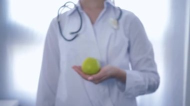 Elinde yeşil elma olan beslenme uzmanı kameraya uzanıyor sağlıklı beslenmeyi tavsiye ediyor, odaklanamıyor.
